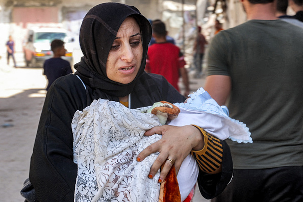 An evacuating woman walks carrying an infant child in the Jabalia camp for Palestinian refugees in the northern Gaza Strip on October 9, 2024 amid the ongoing war in the Palestinian territory between Israel and Hamas. (Photo by Omar AL-QATTAA / AFP) (Photo by OMAR AL-QATTAA/AFP via Getty Images)